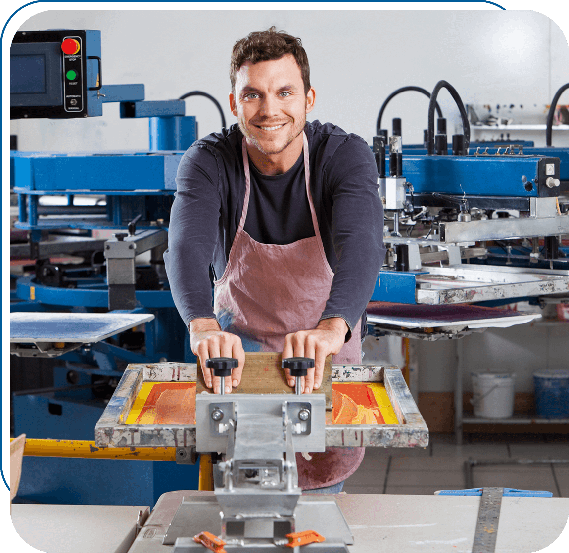 Smiling worker operating a screen printing machine in a workshop